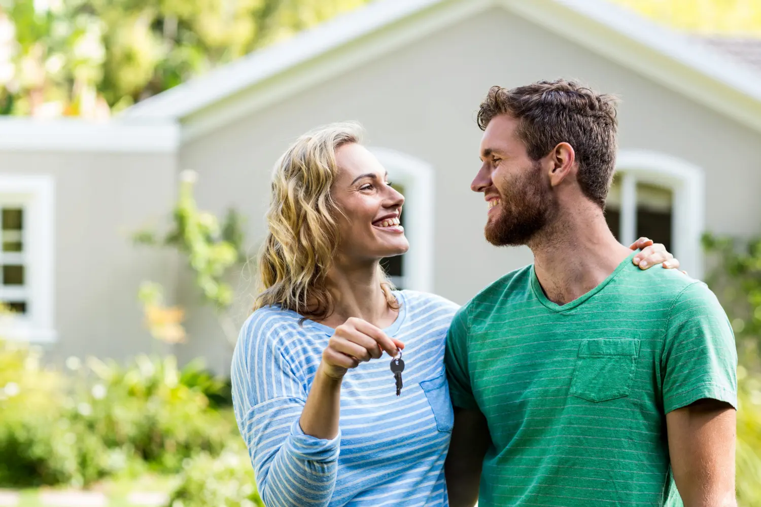 Un couple souriant se tenant devant une maison avec la femme tenant une clé.