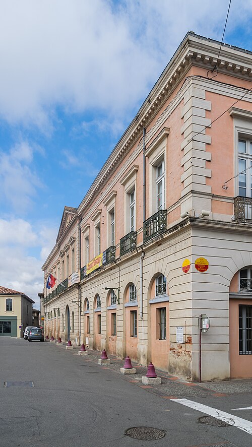 Façade d'un bâtiment administratif historique en pierre beige et rose sous un ciel partiellement nuageux.