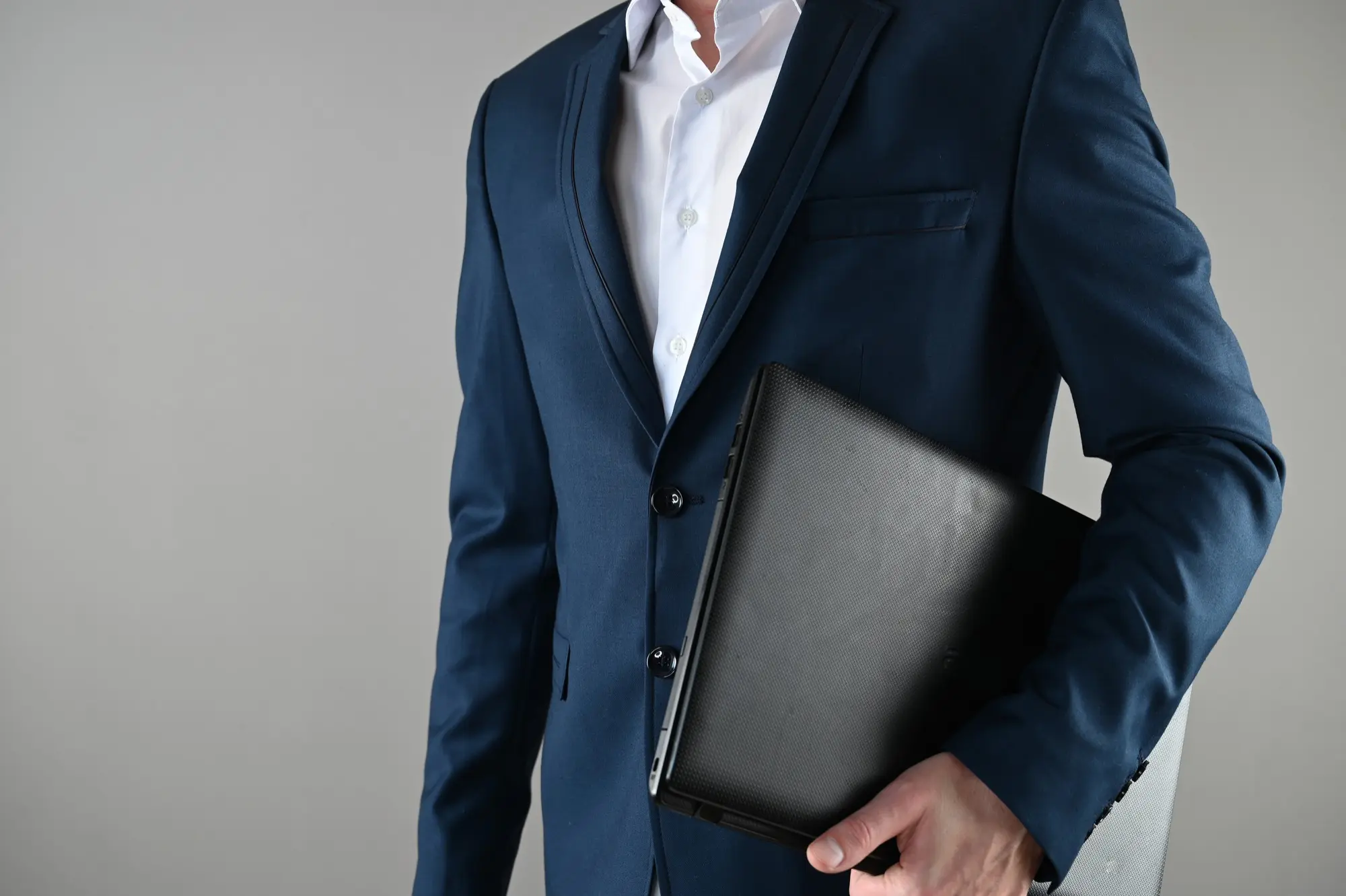 Homme en costume bleu tenant un ordinateur portable noir contre son corps.