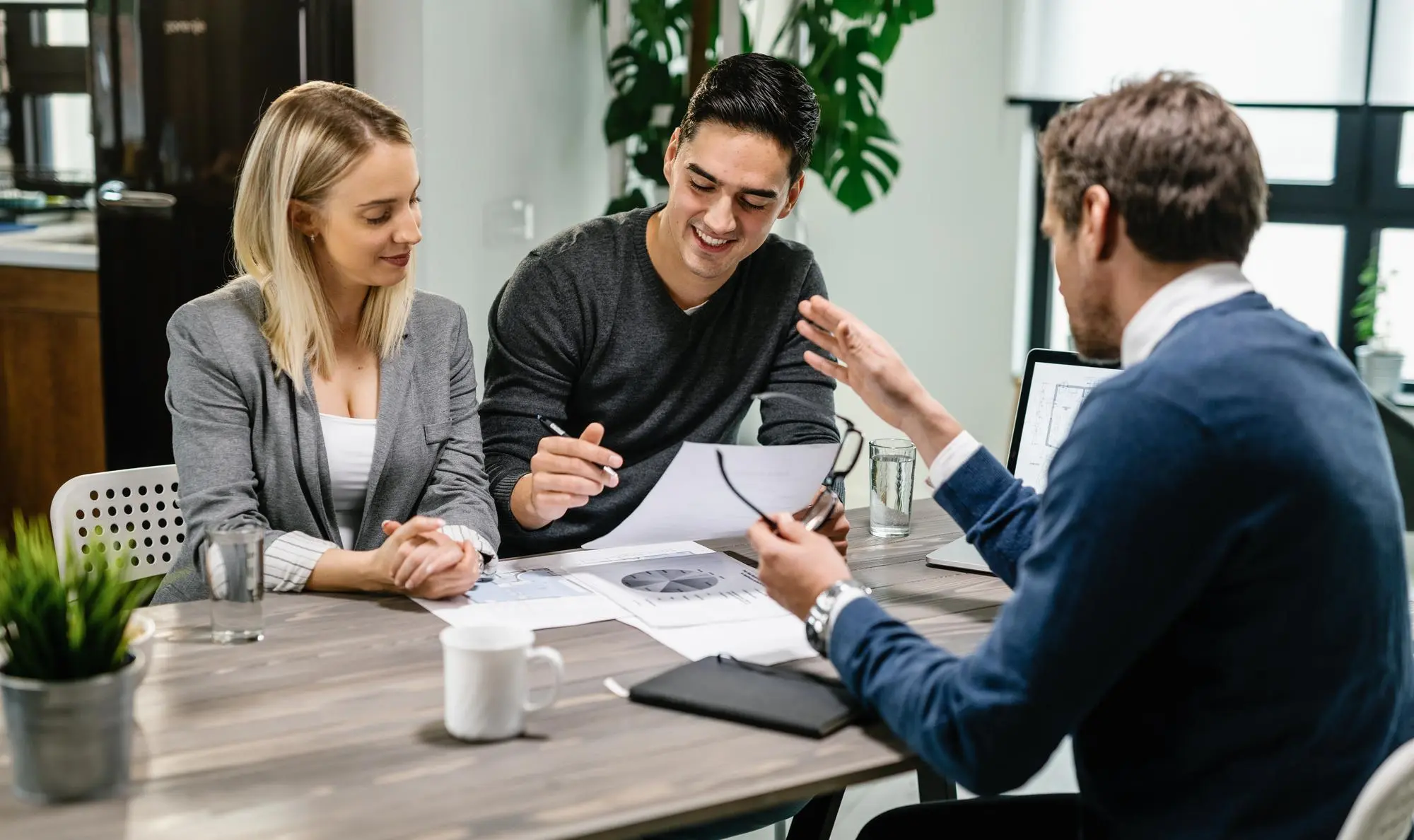 Trois personnes discutant autour d'une table de travail avec des documents et un ordinateur portable.