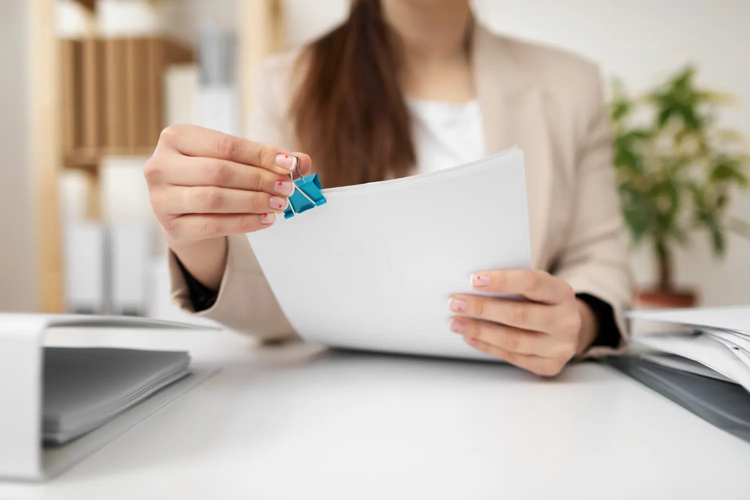 Une personne tenant des feuilles blanches attachées par une pince bleue dans un bureau.