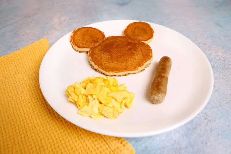 A Mickey Mouse-shaped pancake with your choice of two sides and a drink.