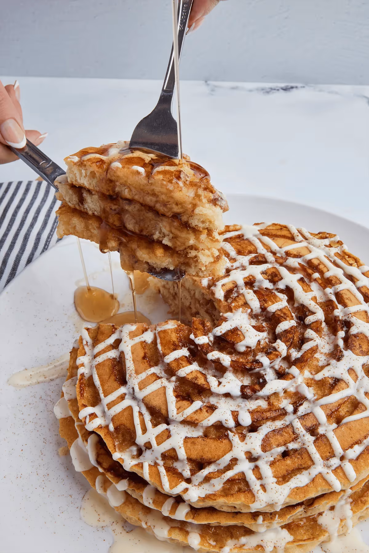 Broken Yolk Cafe cinnamon roll waffle stack with cream drizzle being lifted by fork