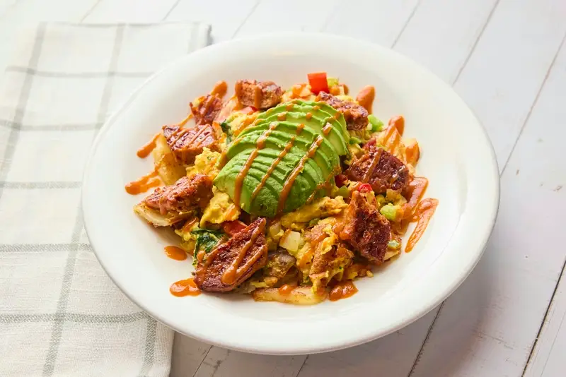 JUST Egg™ scrambled with spinach, mushroom, onion, red and green bell pepper, served over home fries and topped with BEYOND SAUSAGE® hot link, avocado, and sriracha.