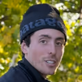Close-up of a man wearing a black Patagonia beanie outdoors with green foliage in the background.