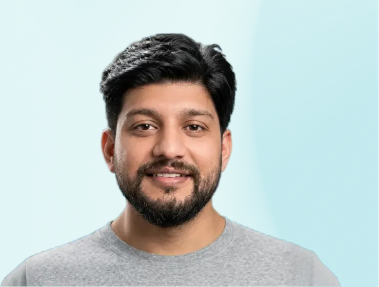 Smiling man with short black hair and beard wearing a gray t-shirt against a turquoise background.
