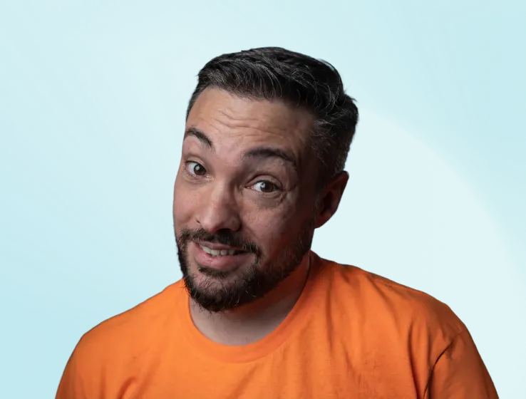 Smiling man with short dark hair and beard wearing an orange shirt against a blue background.