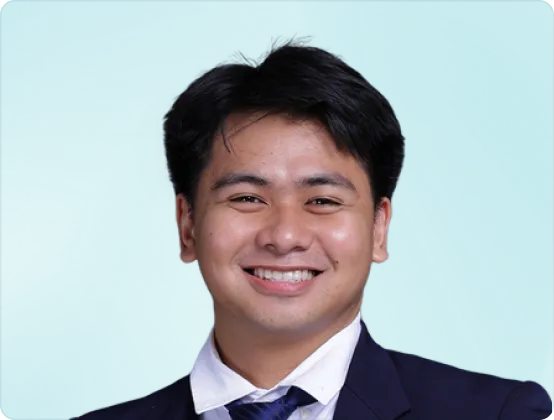 Smiling young man in a dark suit and white shirt against a blue background.