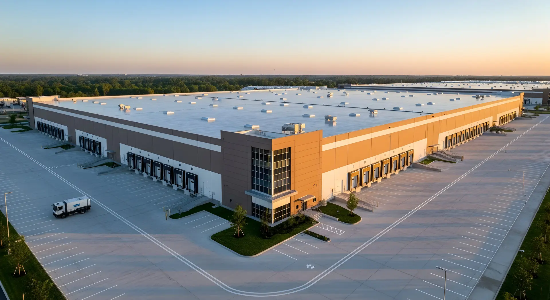 Large modern warehouse building with multiple loading docks and empty parking lots at sunset.