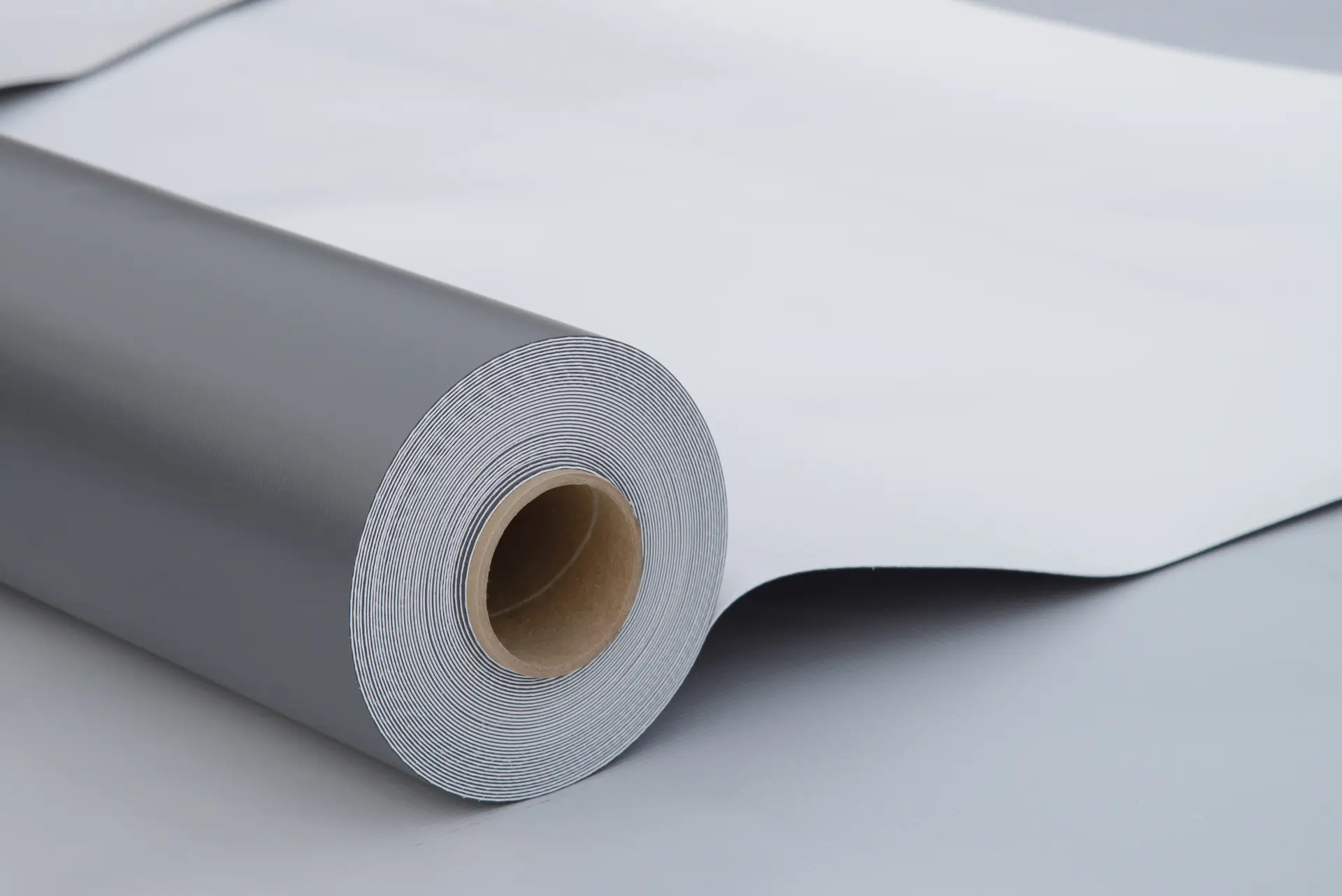 Close-up of a gray roll of vinyl or wallpaper partially unrolled on a flat surface.