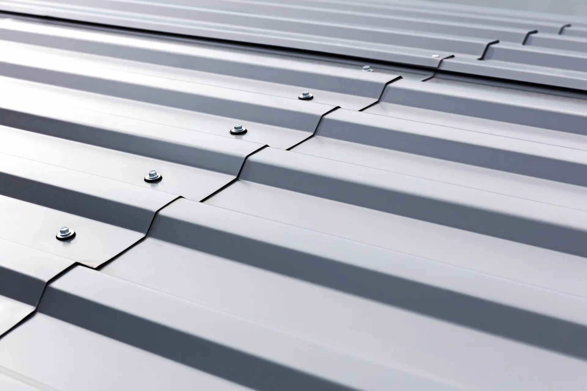 Close-up of a silver metal sheet roof with overlapping panels secured by bolts.