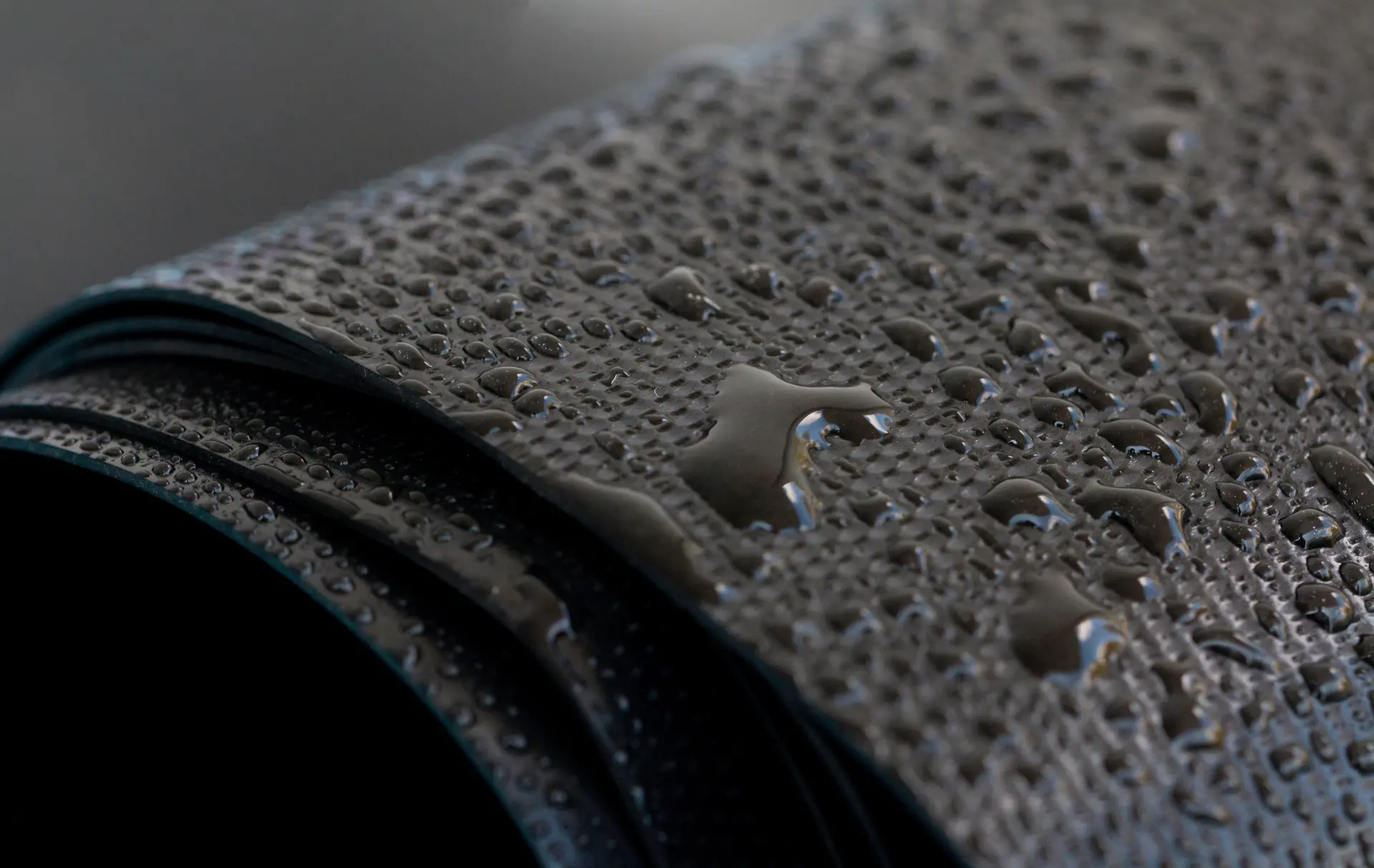 Close-up of water droplets on the textured surface of a rolled-up black rubber mat.