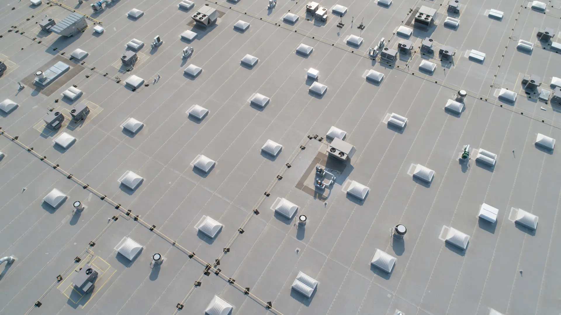 Aerial view of a flat rooftop with multiple skylights, ventilation units, and HVAC systems arranged in rows.