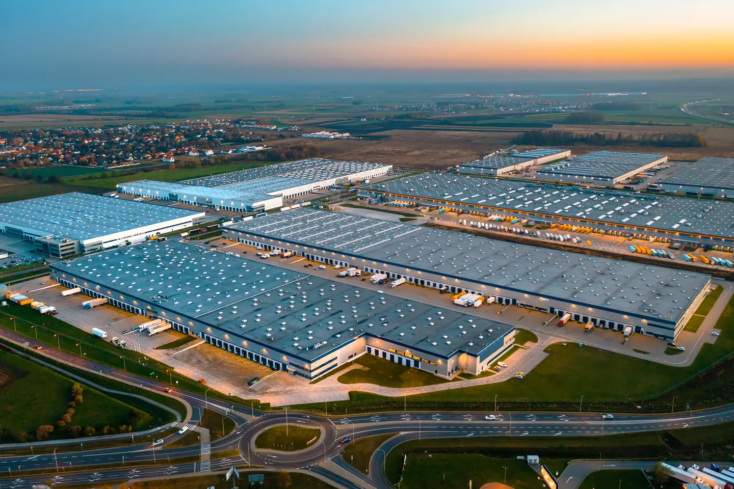 Aerial view of a large industrial warehouse complex with trucks parked outside at sunset.