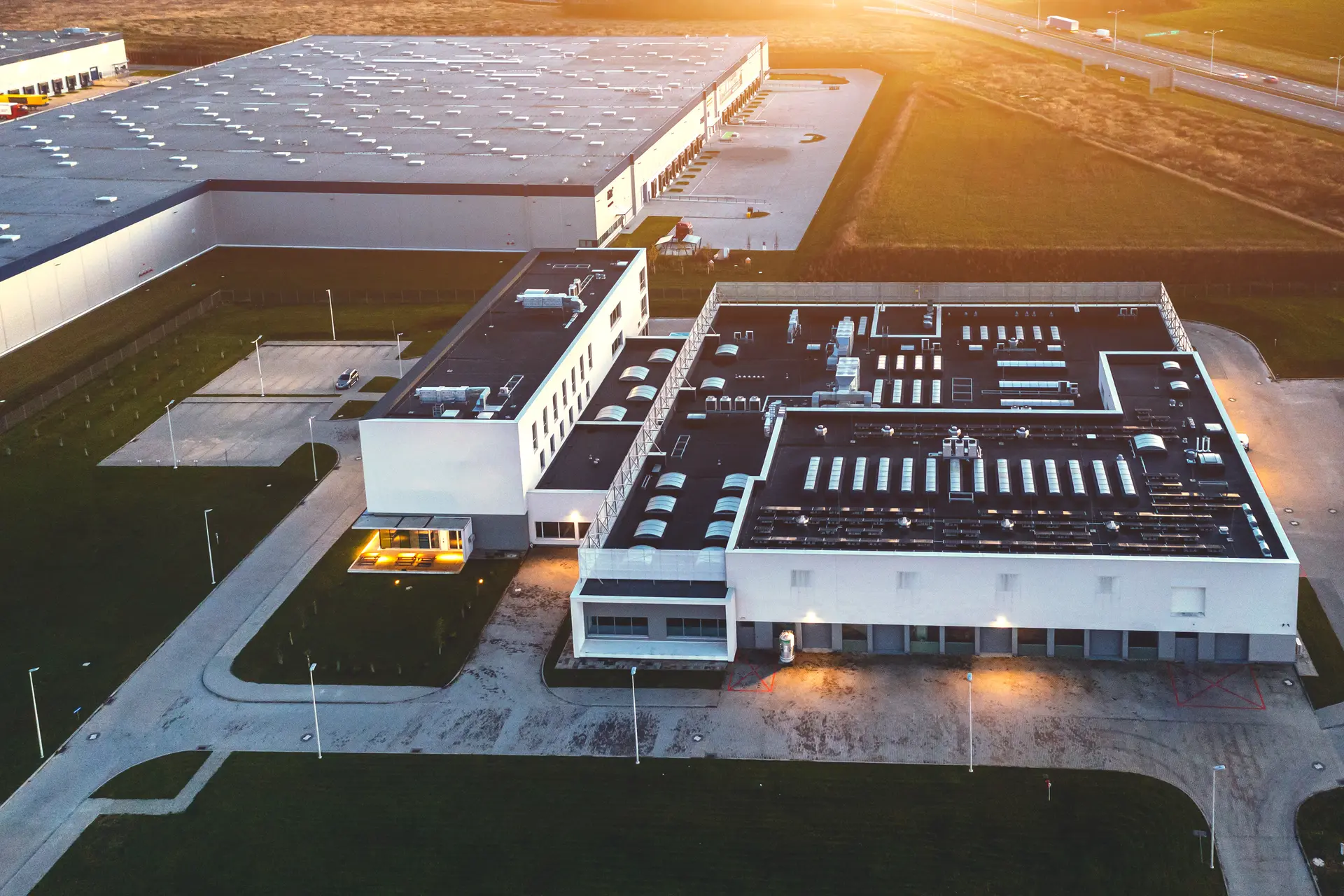 Aerial view of a large industrial warehouse and office building complex at sunset.