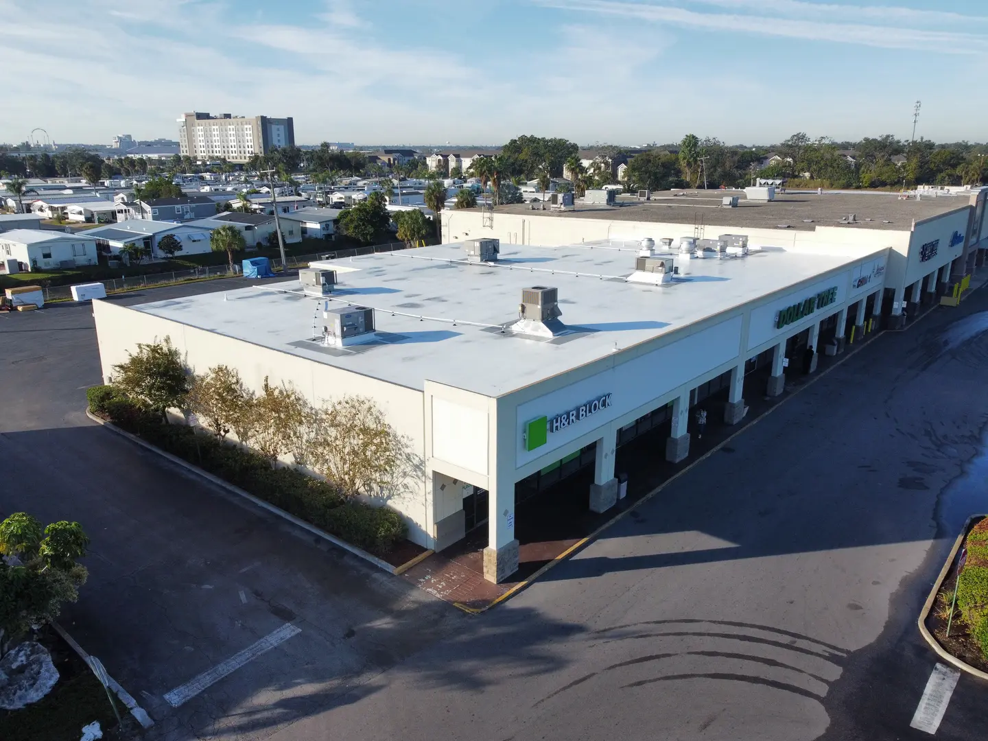 A strip mall with visible store signs for H&R Block and Dollar Tree, surrounded by parking lots and residential buildings in the background.
