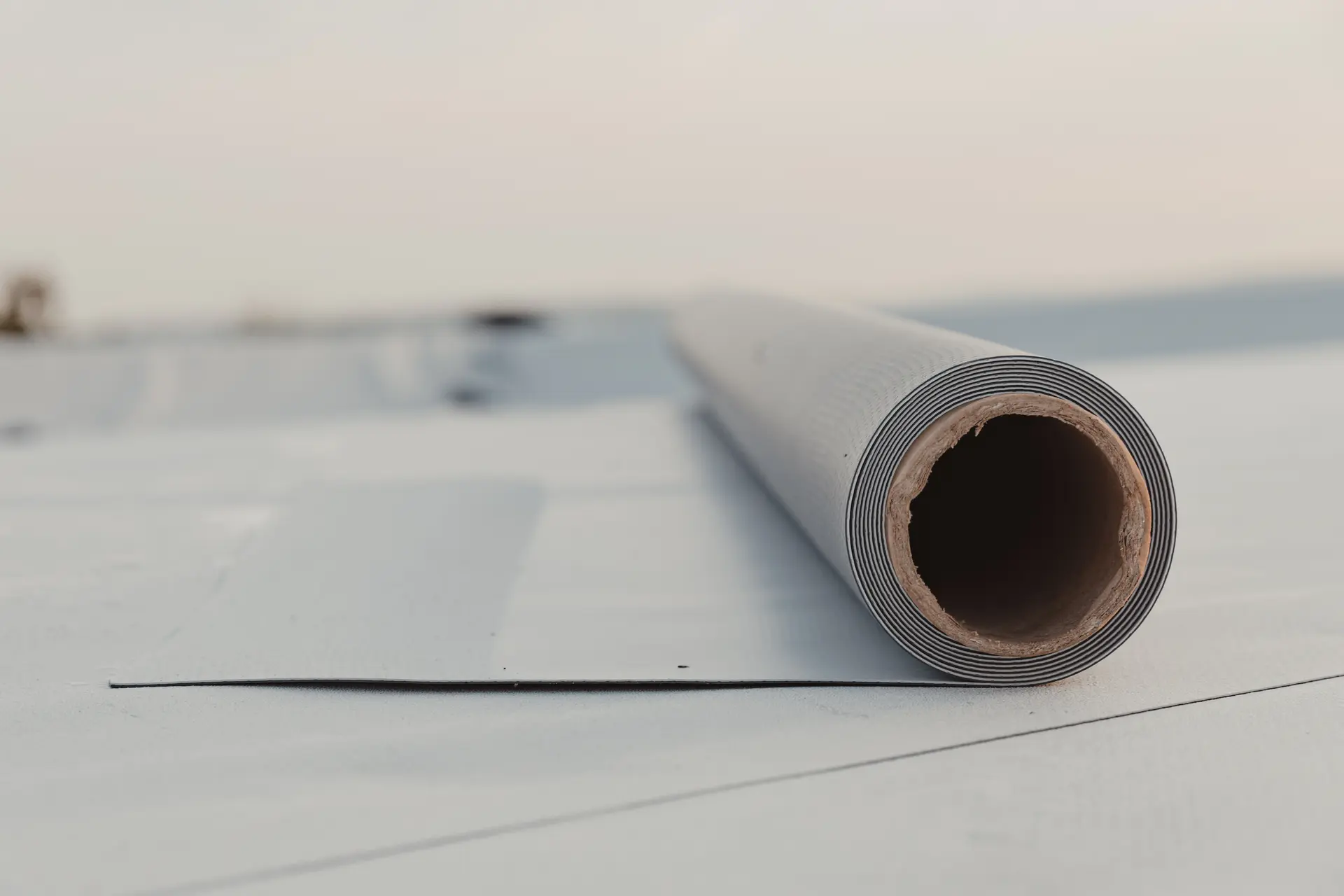 Close-up of a rolled roofing membrane partially unrolled on a flat roof surface.