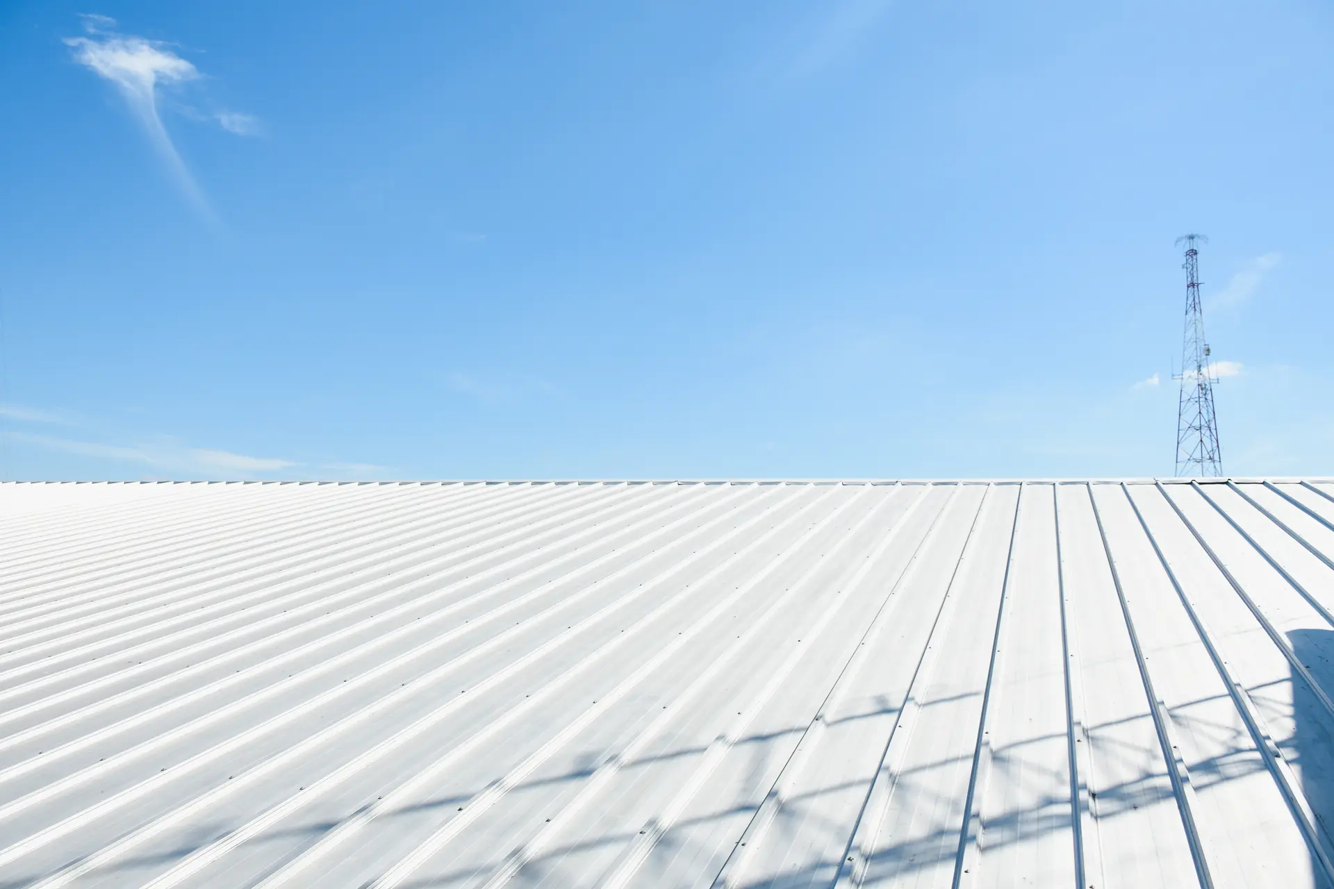 White corrugated metal roof under clear blue sky with a tall communication tower in the distance.