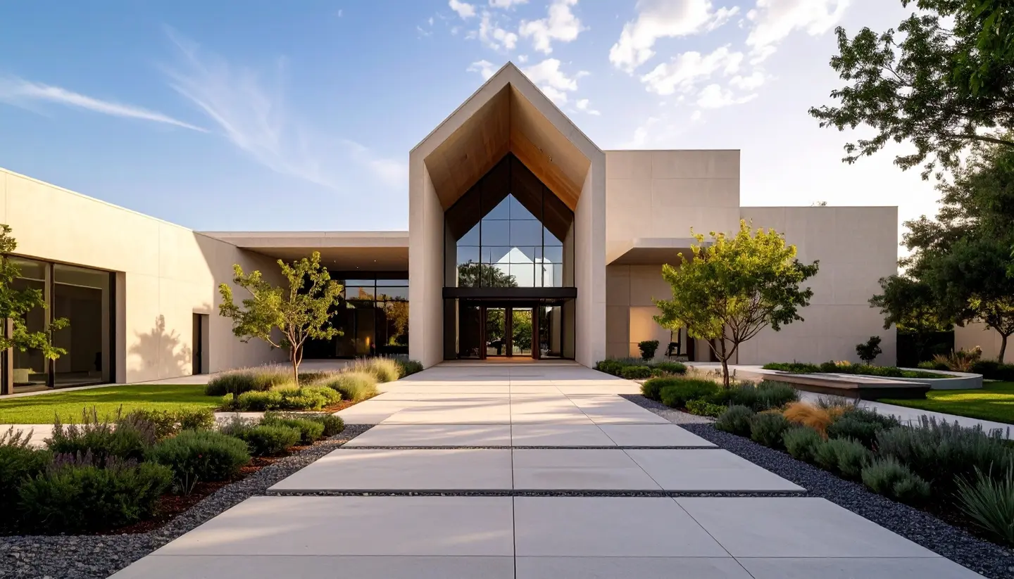 Modern building with a peaked entrance, large glass windows, and landscaped walkway with greenery and trees.