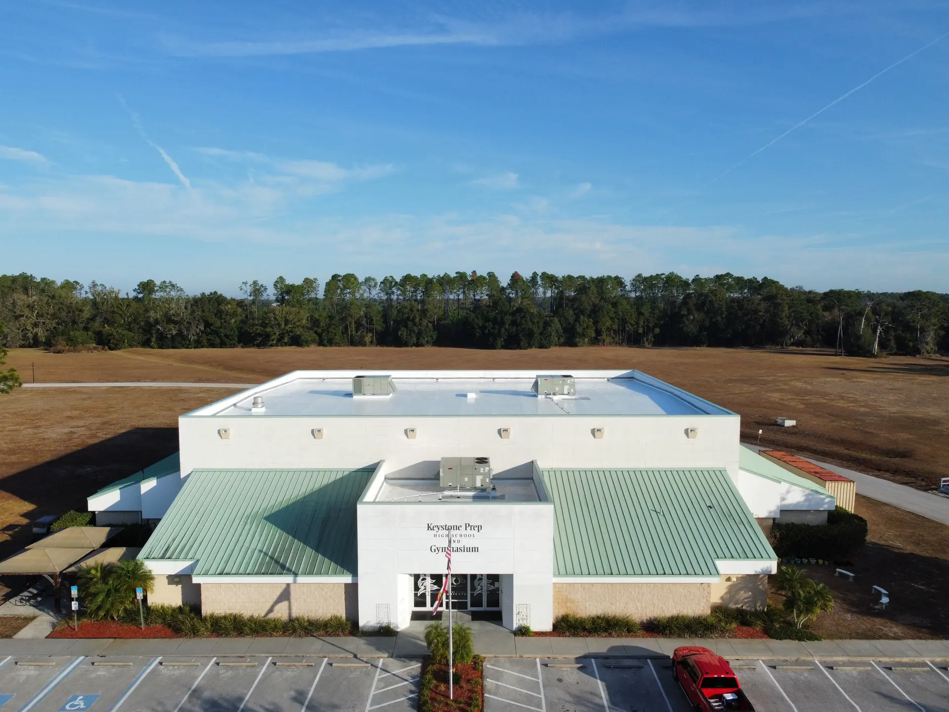 Aerial view of Keystone Prep High School and Gymnasium building with green roofs, parking lot, and surrounding grassy fields.