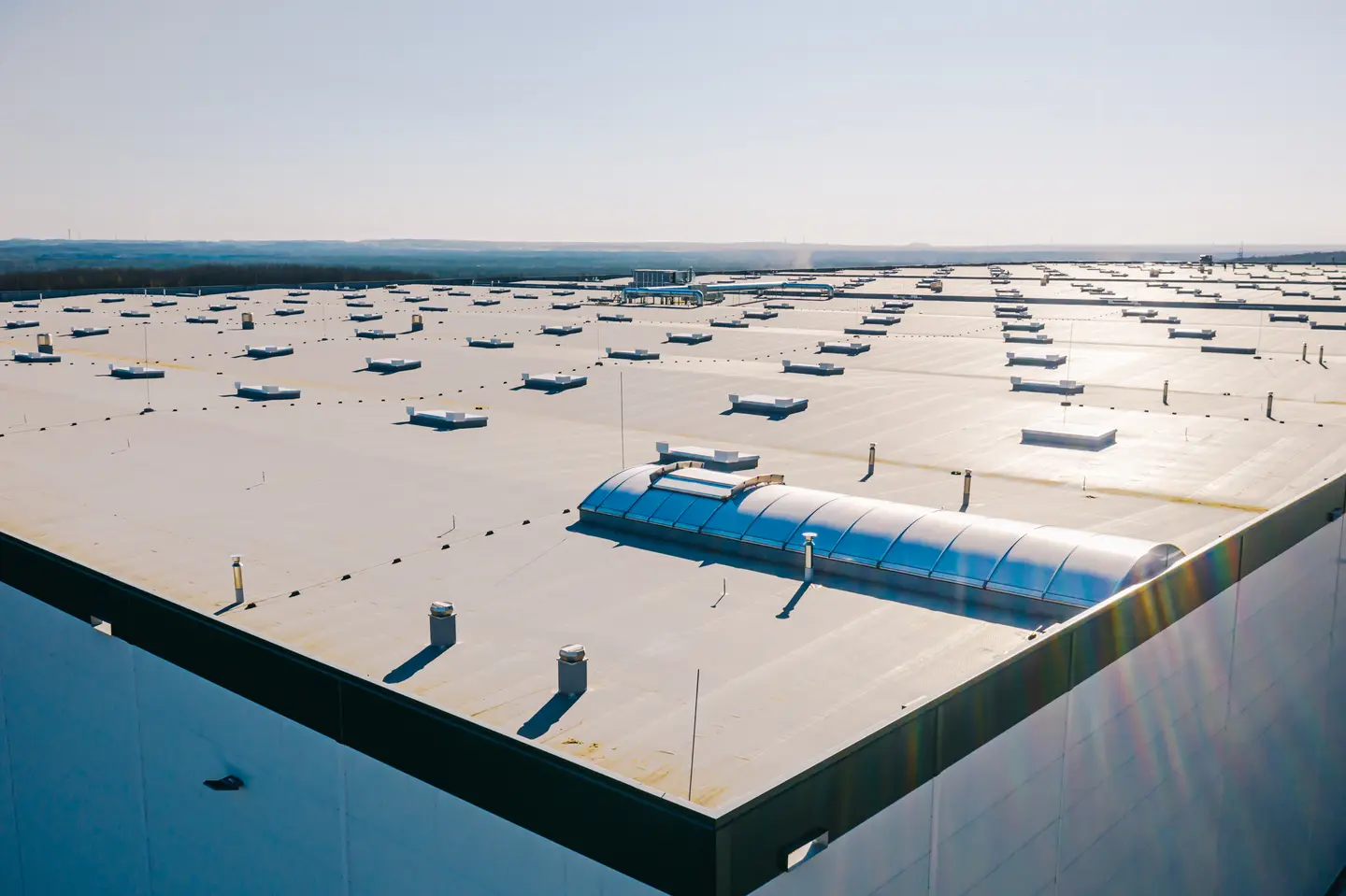 Expansive flat roof of an industrial building with numerous vents and skylights under a clear sky.