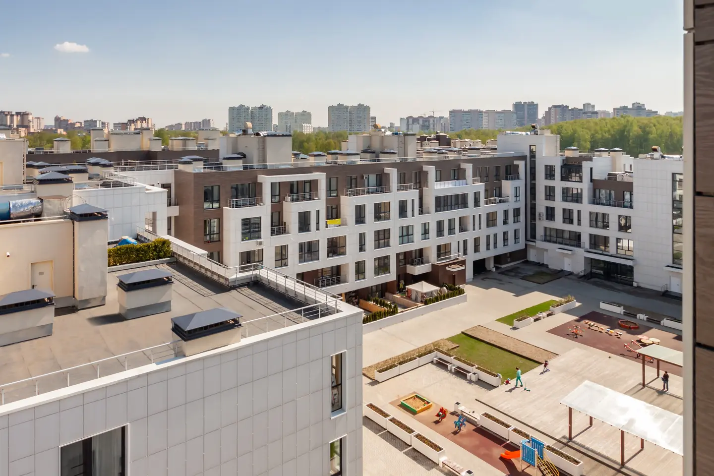 Modern residential apartment complex with a central courtyard featuring playground, garden beds, and a few people walking.