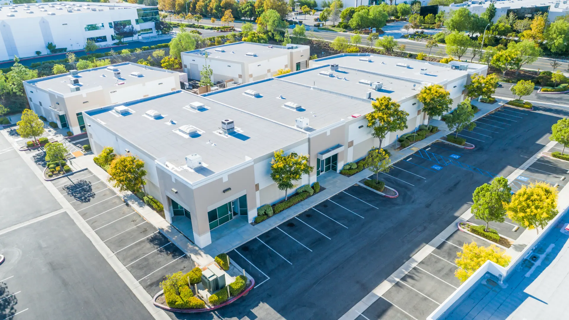 Aerial view of multiple modern commercial warehouse buildings with empty parking lots and surrounding greenery.