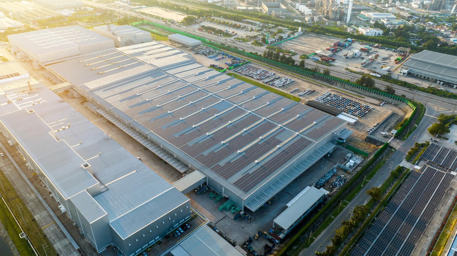 Aerial view of a large industrial facility with solar panels installed on the rooftops and parked cars in adjacent lots.