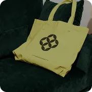 Yellow branded tote bag with BB logo resting on green grass