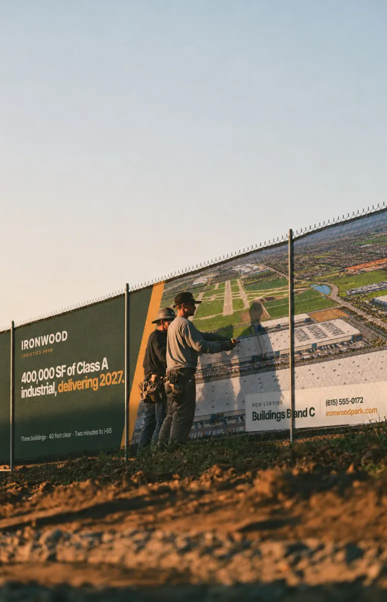 Two workers standing at an Ironwood fence wrap advertising 400,000 square feet of Class A industrial space