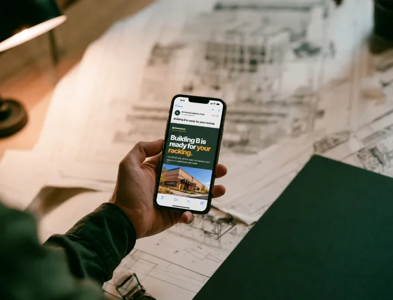 Hand holding a phone showing an email about Building B over printed site plans