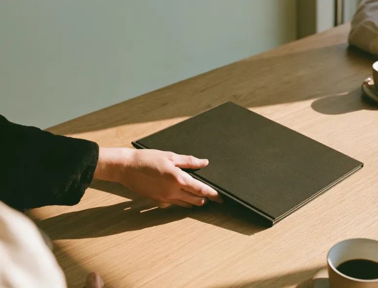 Hand placing a dark green pitch deck on a wooden table next to a coffee cup