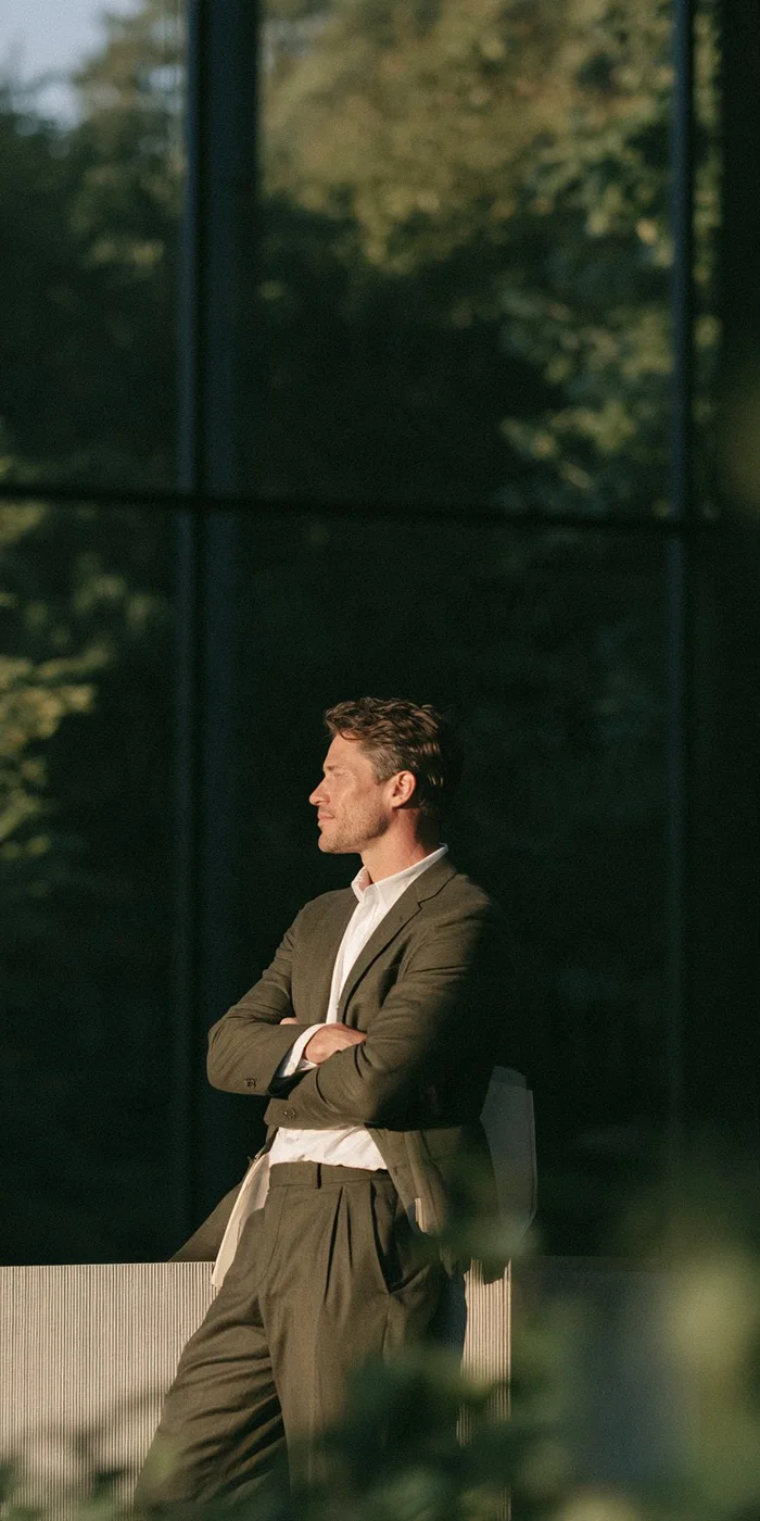 Broker leaning against a window in a dim office lobby