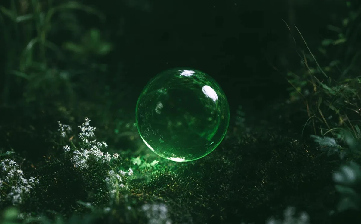 Green glass sphere resting in dark moss and small white flowers