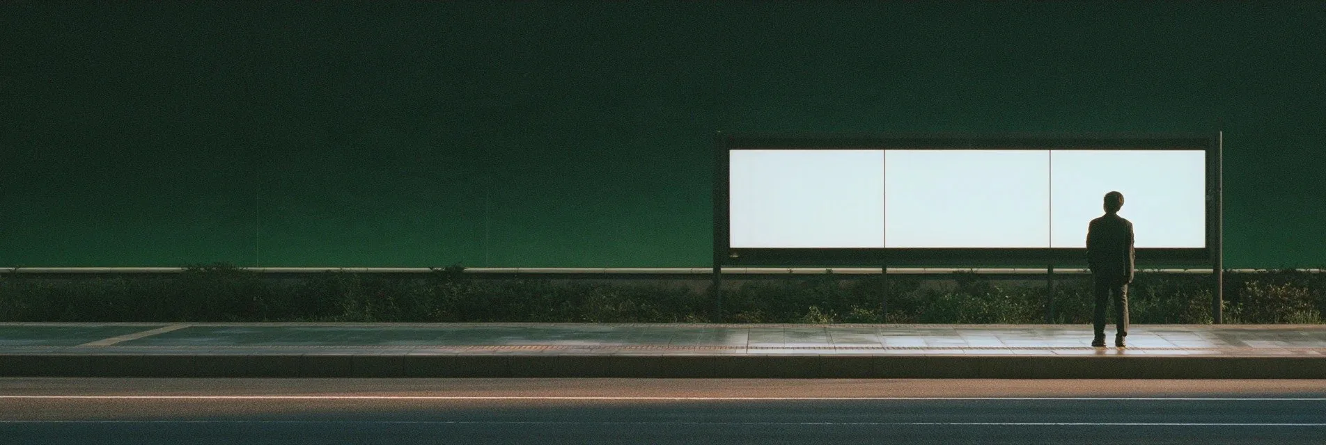 Person standing in front of a long lit panel on a quiet road at night