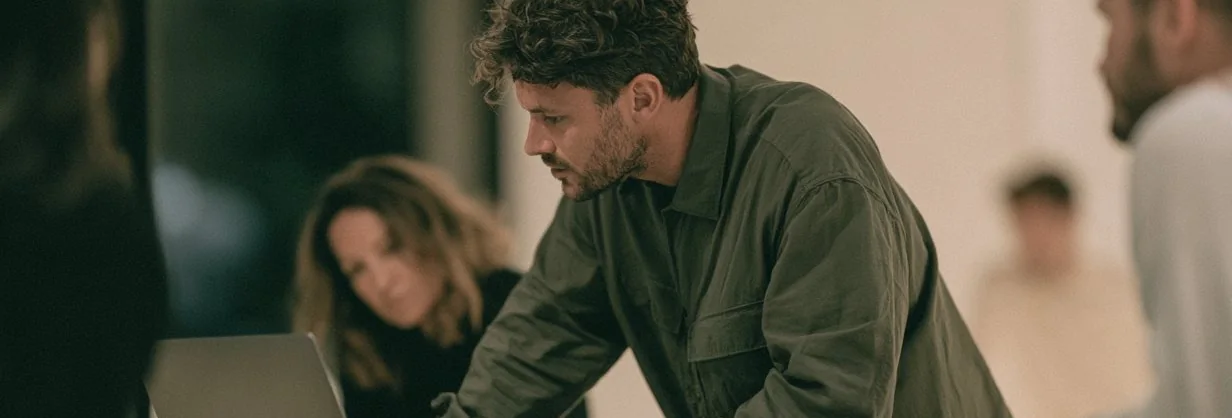 Man leaning over a work table with colleagues behind him