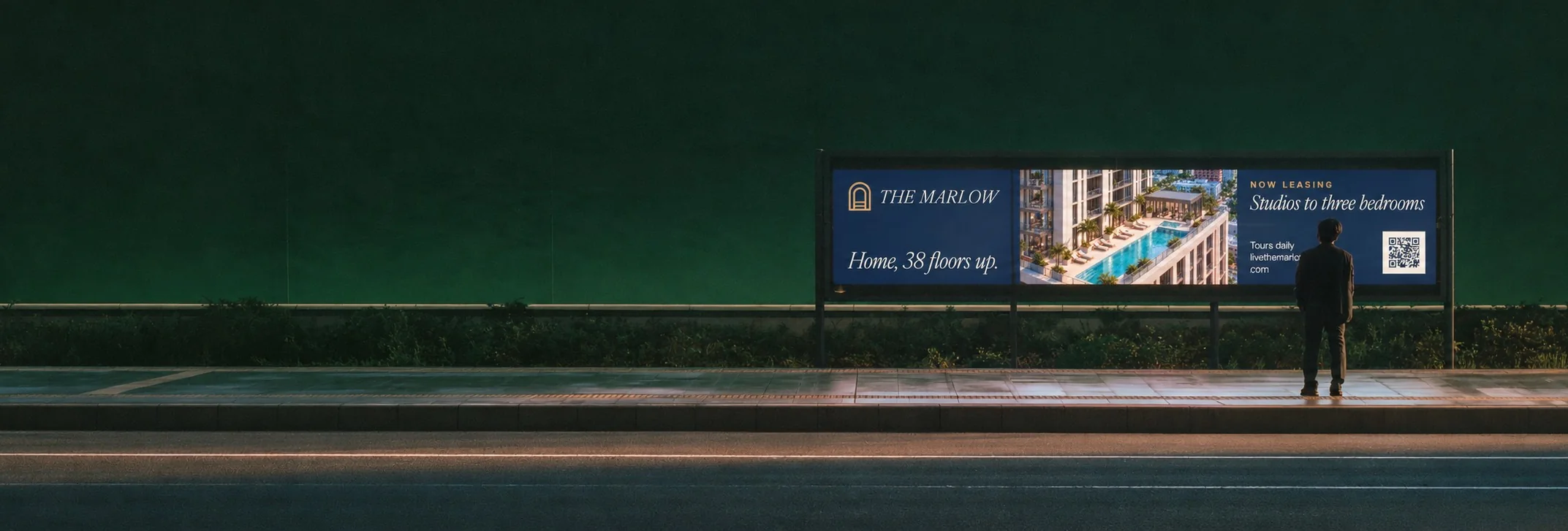 Person standing under a lit billboard for The Marlow apartments at night