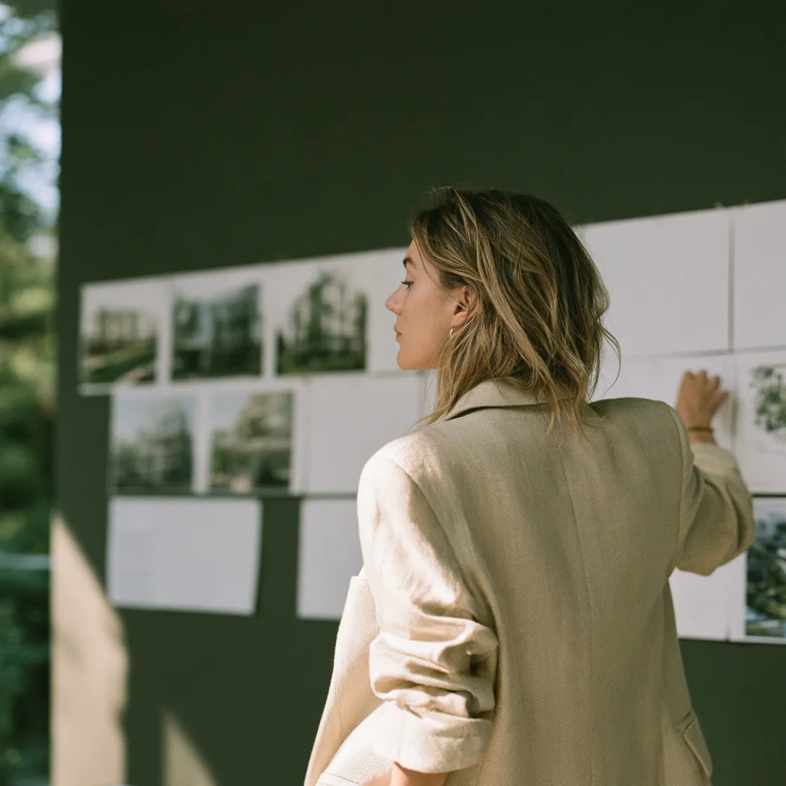 Woman in a linen blazer reviewing a wall of pinned building photos and printed pages