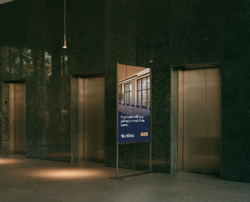 Building lobby with bronze elevator doors and a digital sign stand showing an office leasing ad