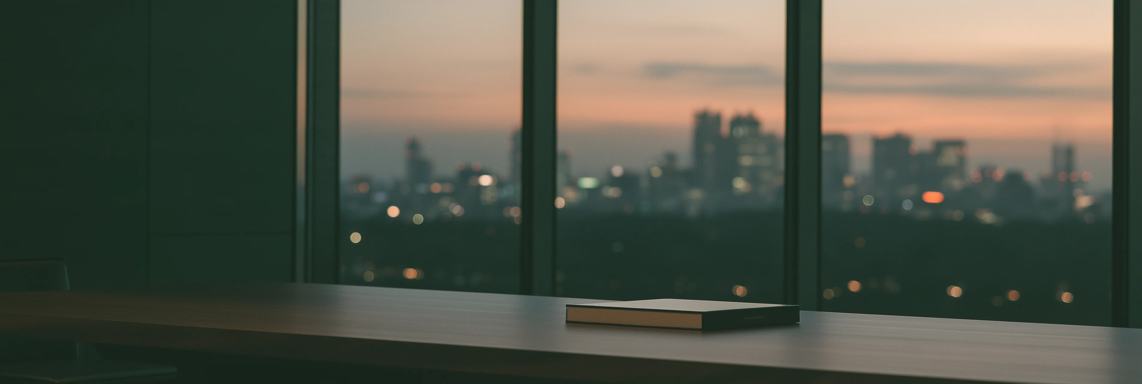 A closed presentation book on a long boardroom table at dusk, city lights through the windows