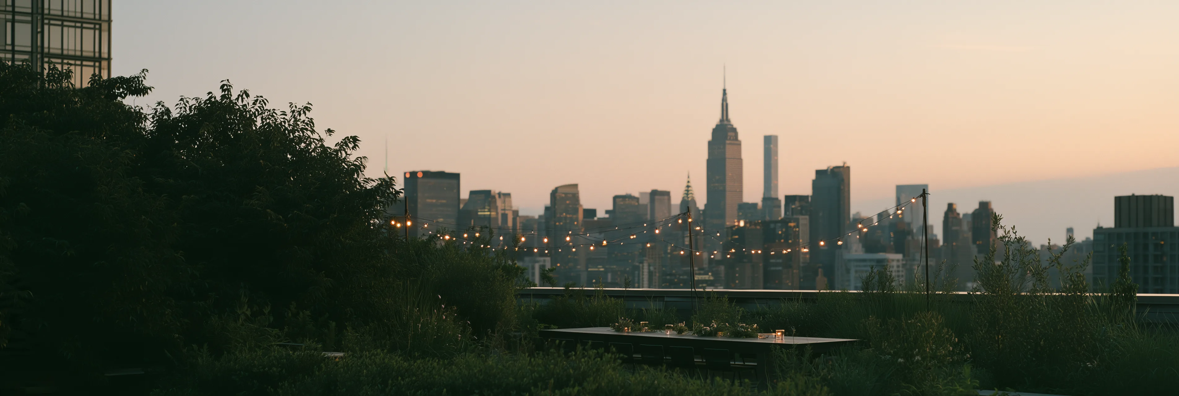 A rooftop terrace set for an evening reception, with the city skyline at dusk beyond
