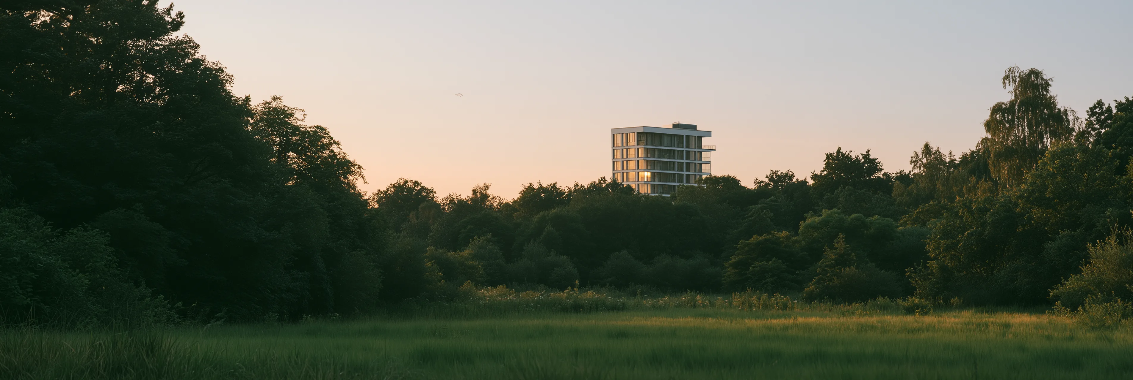 A new apartment building at dusk with warm lit windows, seen across a quiet park