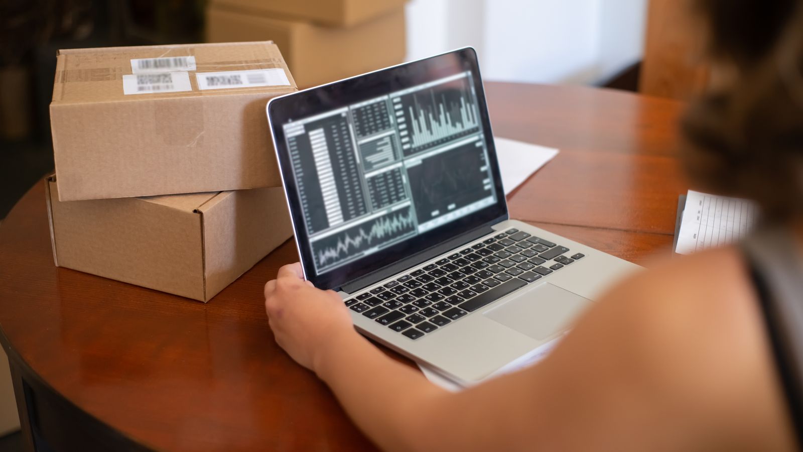 Entrepreneur e-commerce analysant les données de suivi de sa boutique sur un ordinateur portable, à côté de colis prêts à expédier
