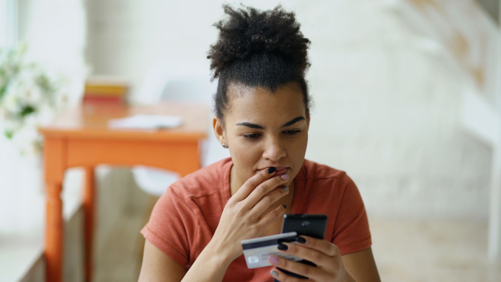 Cliente hésitant devant son téléphone et sa carte bancaire au moment de payer, situation typique d'un panier abandonné en e-commerce