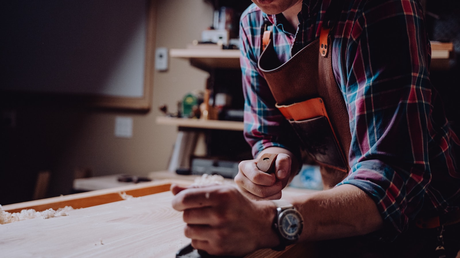 Menuisier en tablier de cuir rabotant une planche dans son atelier