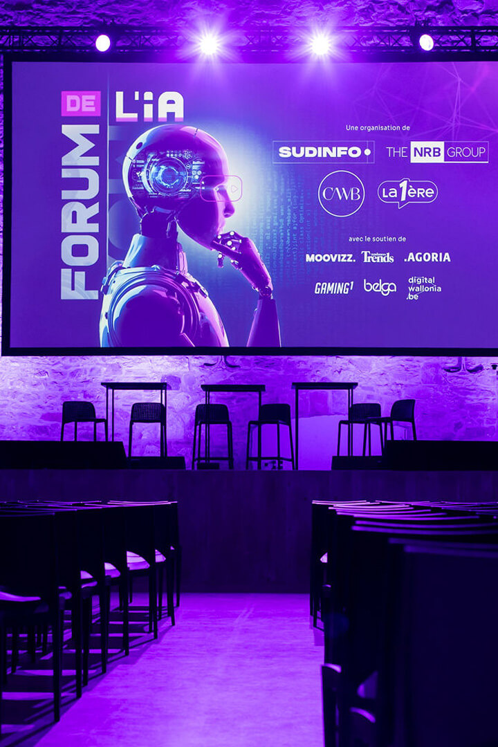 Scène du Forum de l’IA avec écran géant et éclairage violet avant conférence
