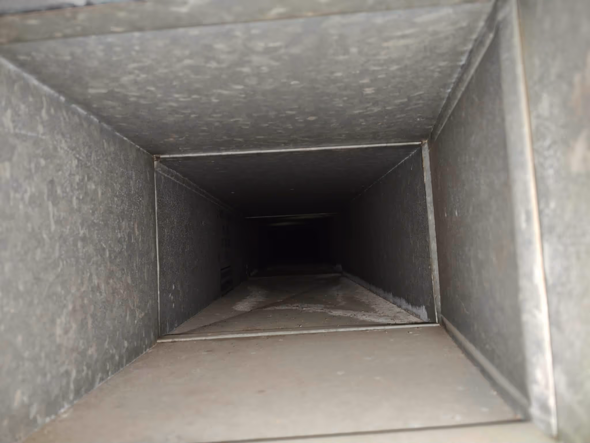 Inside view of a dark rectangular metal air duct vent tunnel.