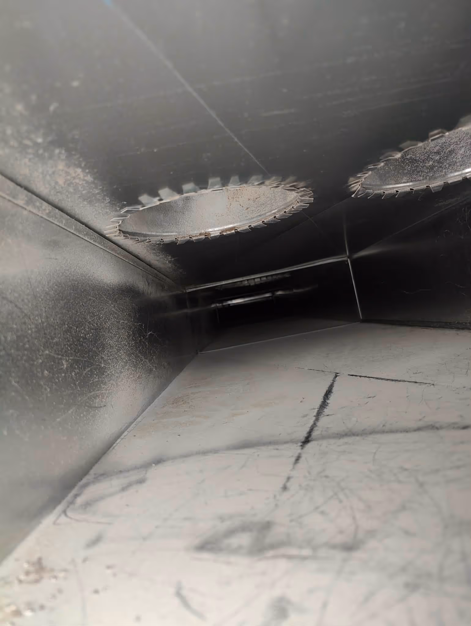 Inside view of a rectangular metallic duct with two circular saw blades mounted on the ceiling.