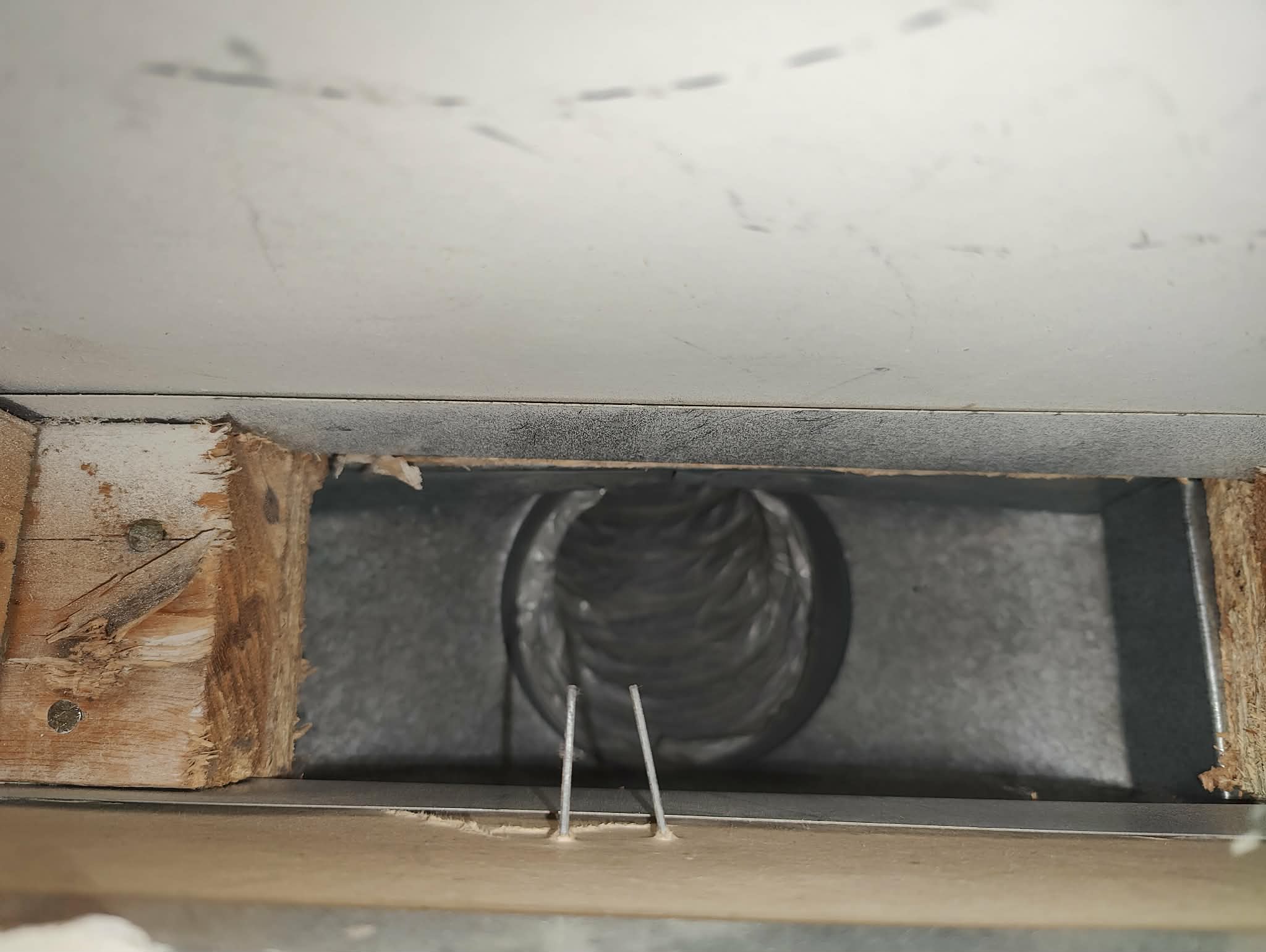 Rectangular vent opening with exposed wood framing and a black flexible duct inside.