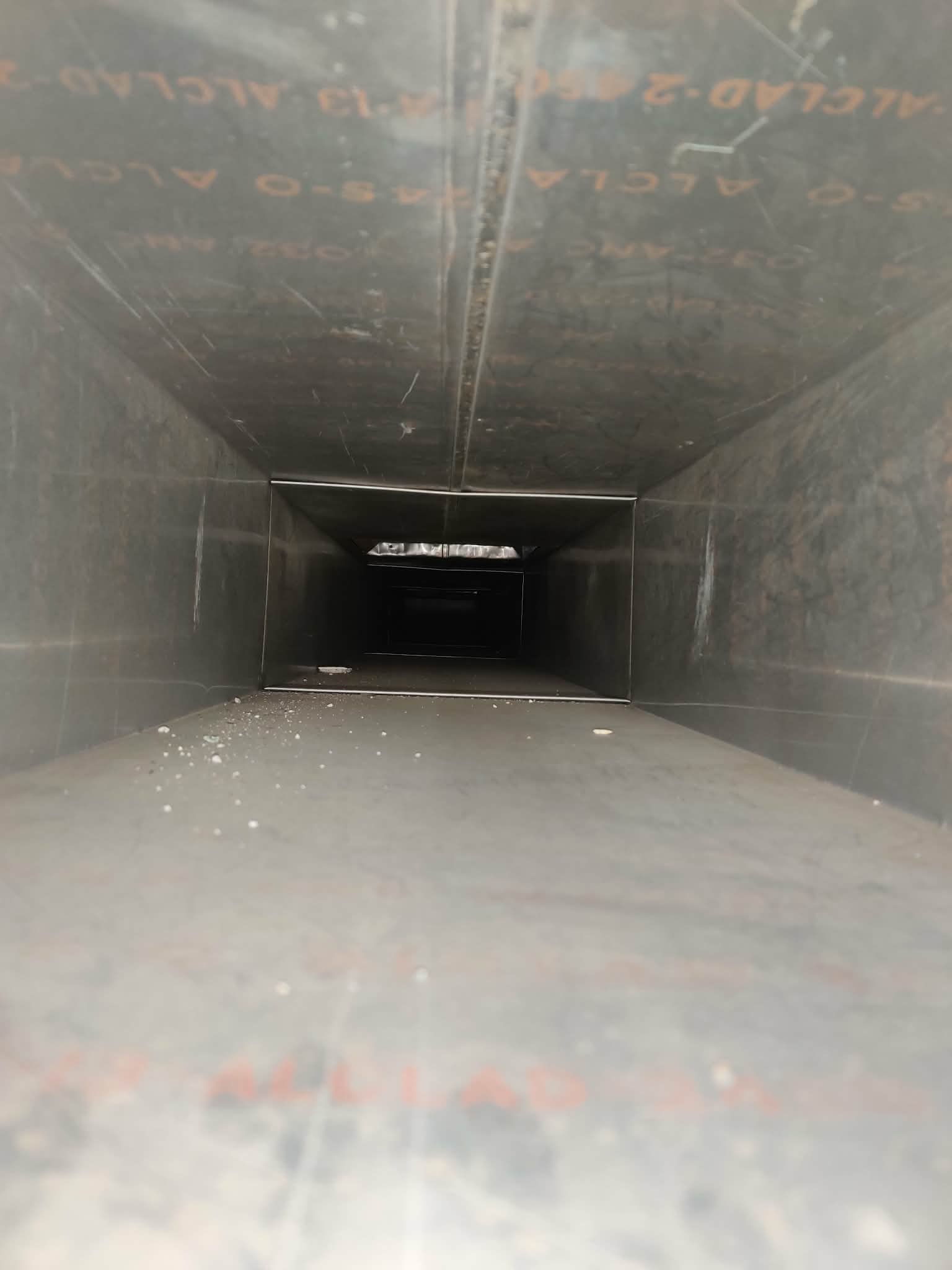 Inside view of a long rectangular metal duct with some dust and markings on its inner surface.